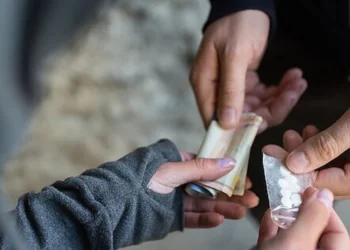 Paauglys laiko išmanųjį telefoną tamsiame kambaryje, žiūrėdamas į žinutes programėlėje