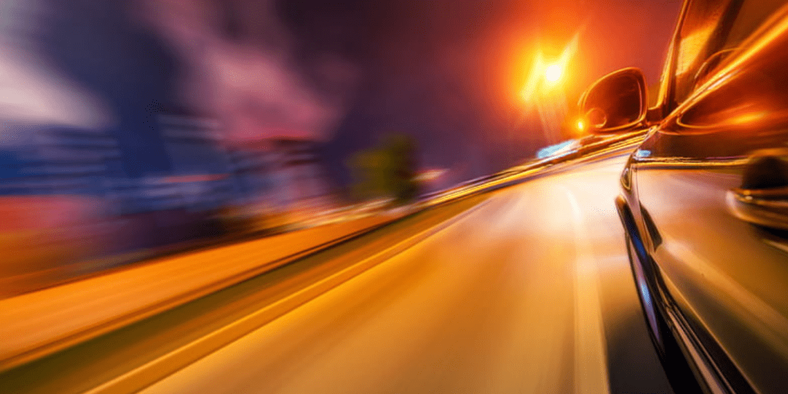 Automobiliai su ryškiomis žibintų šviesomis naktinėje miesto gatvėje
