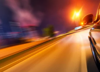 Automobiliai su ryškiomis žibintų šviesomis naktinėje miesto gatvėje