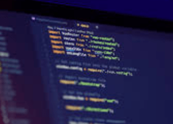 Programuotojas prie kompiuterio ekrano su programavimo kodu, simbolizuojantis etišką įsilaužimą