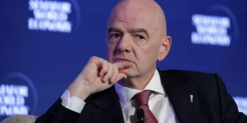 FIFA prezidentas sveikinasi su minia futbolo stadione, aplink žurnalistai su kameromis
